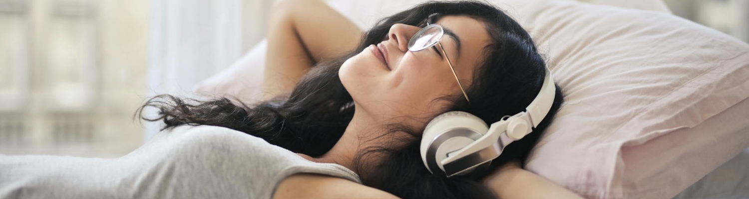 a woman in bed listening to musing using the headphones 